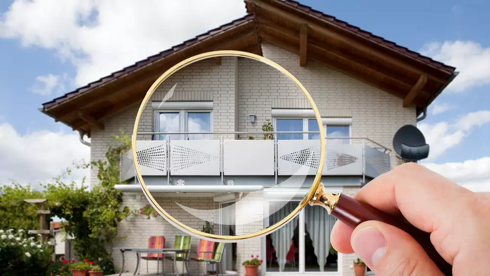 A hand holds a magnifying glass up against the back of a two-story house.