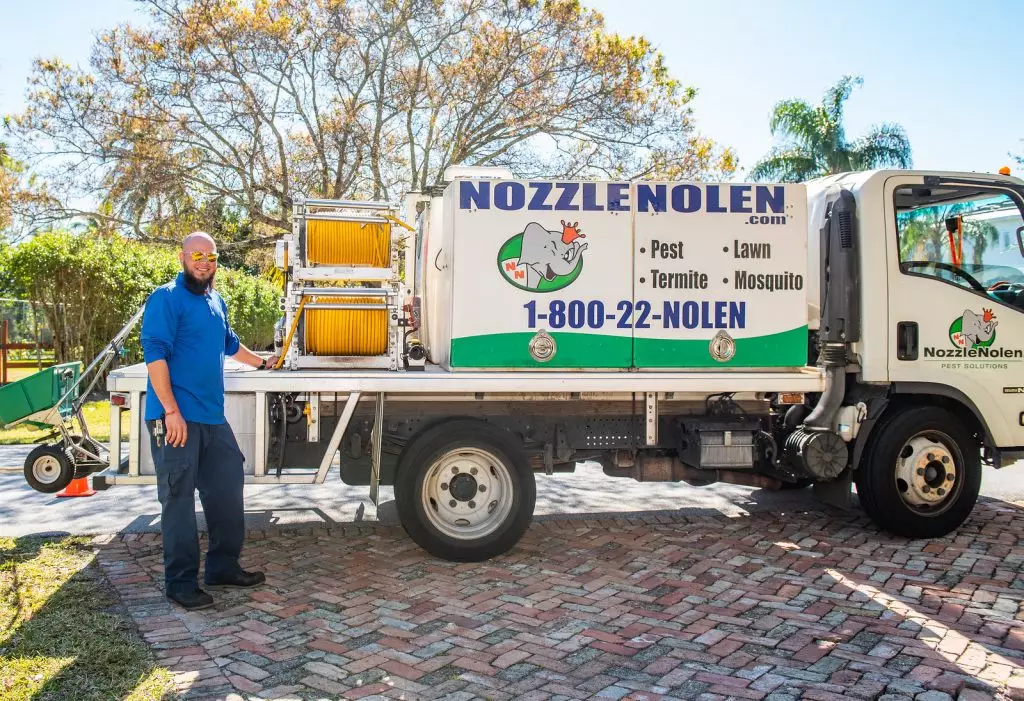 A Nozzle Nolen employee is standing next to a commercial lawn care services vehicle.