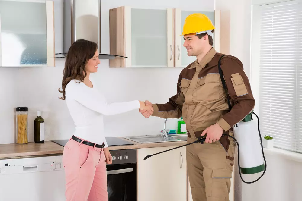 A happy customer shakes hands with a pest control technician in her kitchen