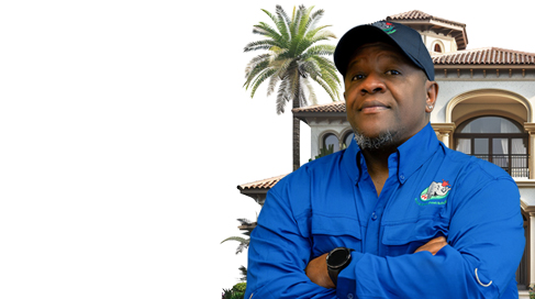 A person in a blue shirt and cap, arms crossed, stands confidently in front of a large house with a palm tree in the background.