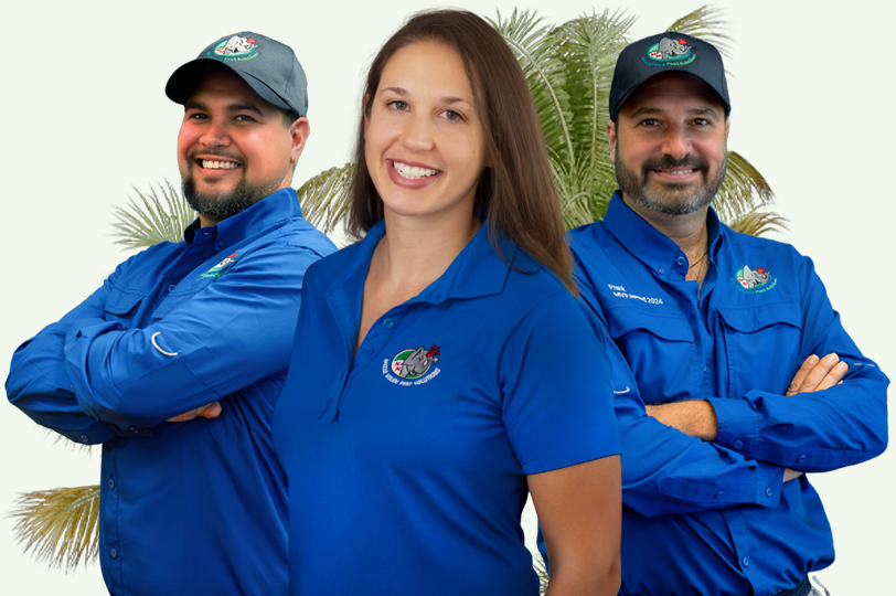 Three people wearing blue shirts and caps with a logo stand smiling in front of palm trees. The two men have beards, and they stand on either side of a woman with long hair. They all have their arms crossed.