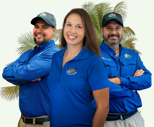 Three individuals wearing blue polo shirts and caps with embroidered logos stand smiling in front of palm trees. Two men with beards flank a woman with long brown hair in the center. They all appear to be part of the same team or organization.